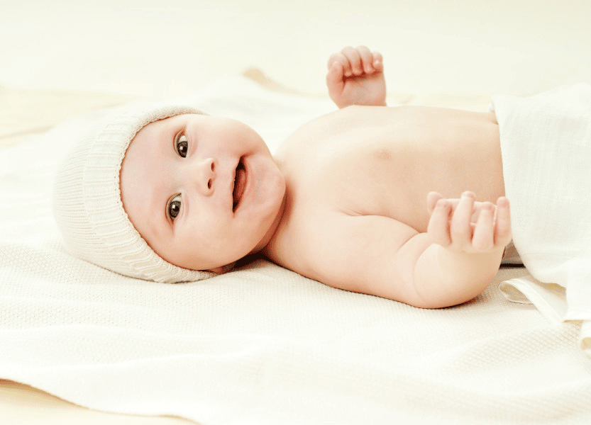 Happy baby lying on back smiling.