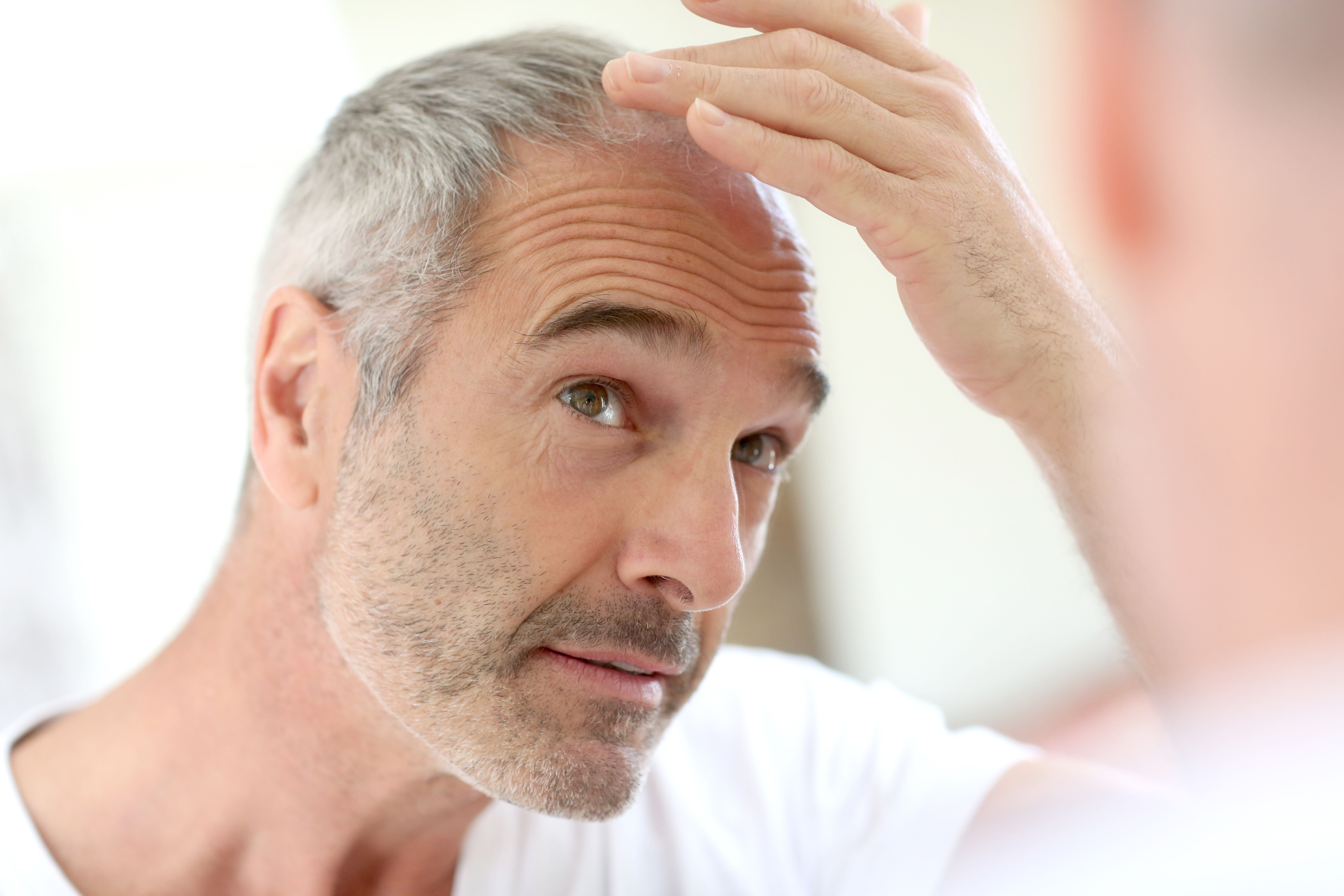 Homme chauve et d'âge mur regardant sa ligne de cheveux dans le miroir