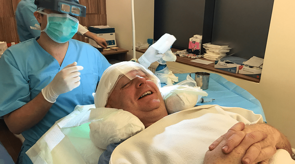 Patient lying down and smiling while preparing to undergo a FUE hair transplant.