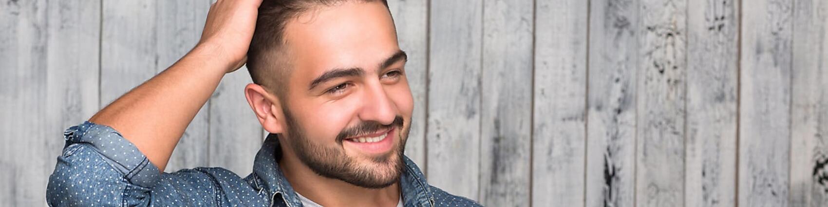 Smiling man rubs hand through his new hair following his hair transplant surgery.