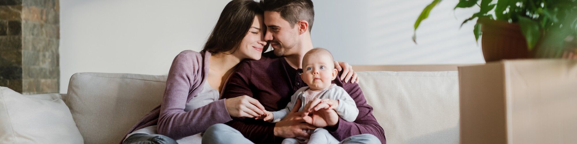 Happy couple smiling and sitting on the sofa holding baby.