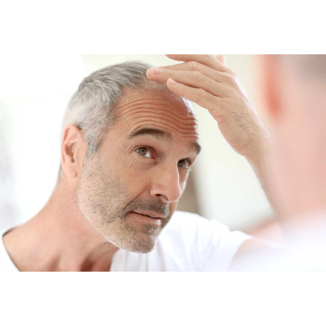 Older balding man looking in the mirror at his hairline